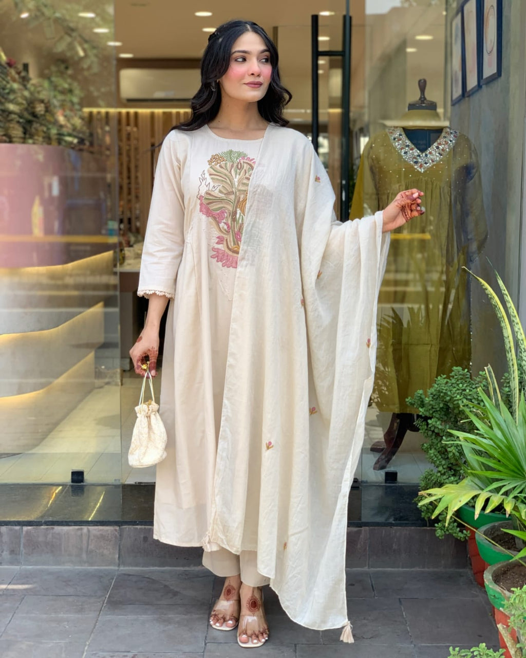 Woman in a white traditional outfit standing in front of a store with mannequins.