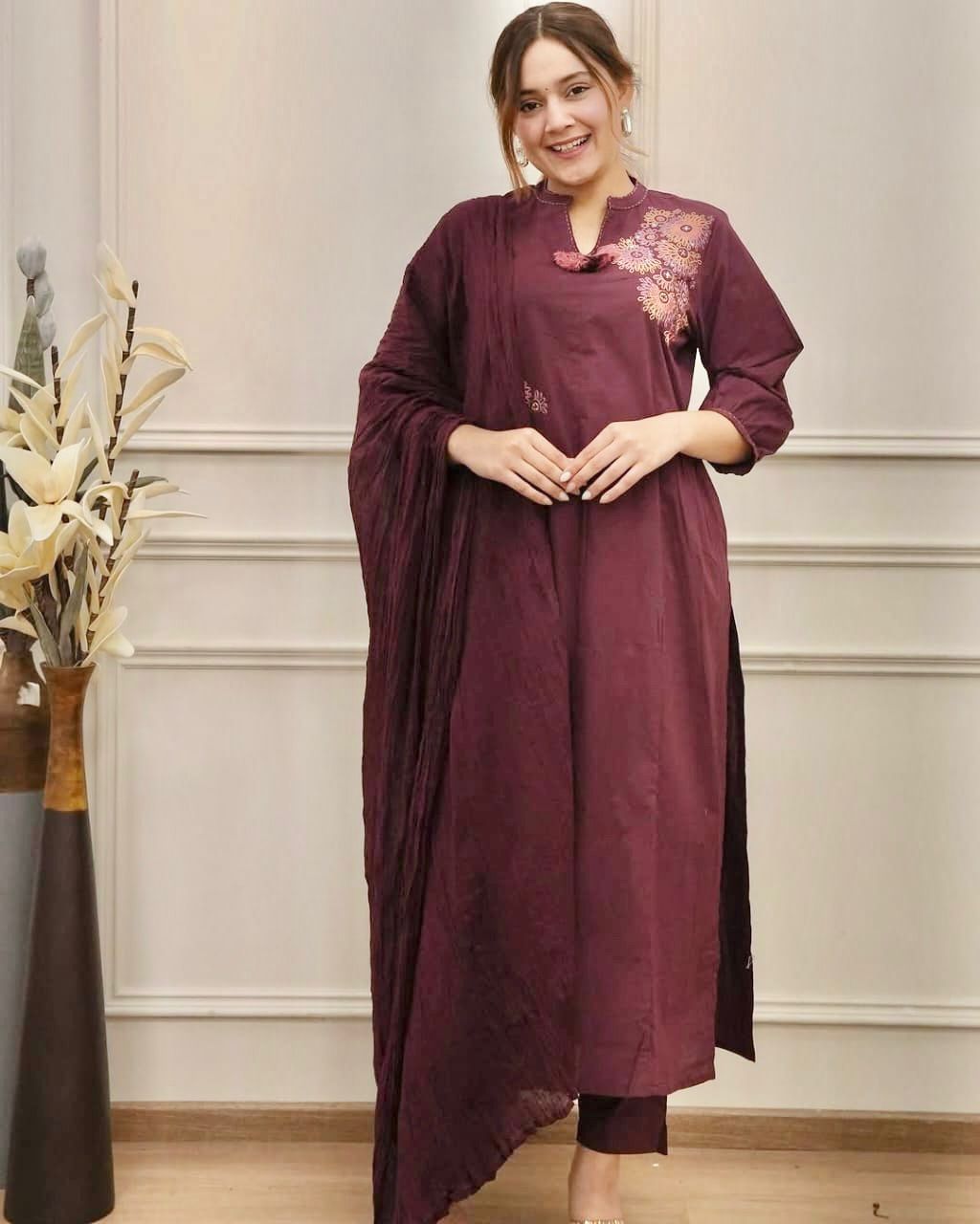 Woman wearing a maroon kurta with floral embroidery in a room with decorative elements.