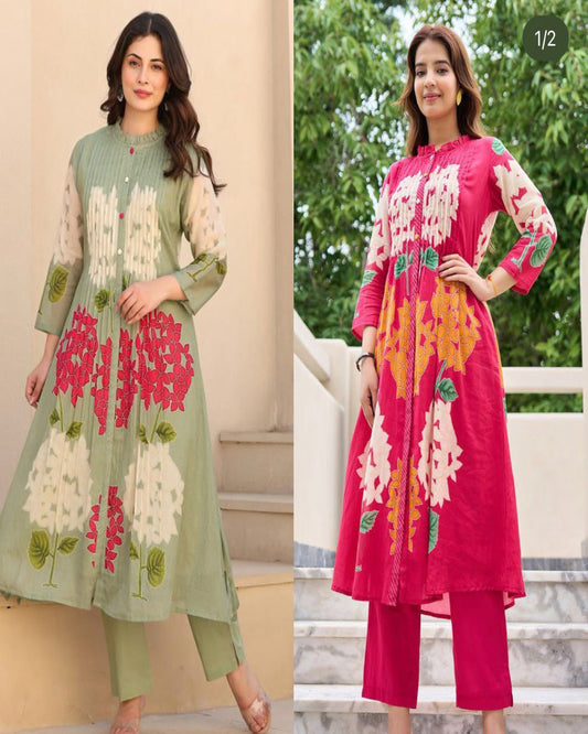 Two women wearing floral embroidered outfits with a neutral background and greenery.