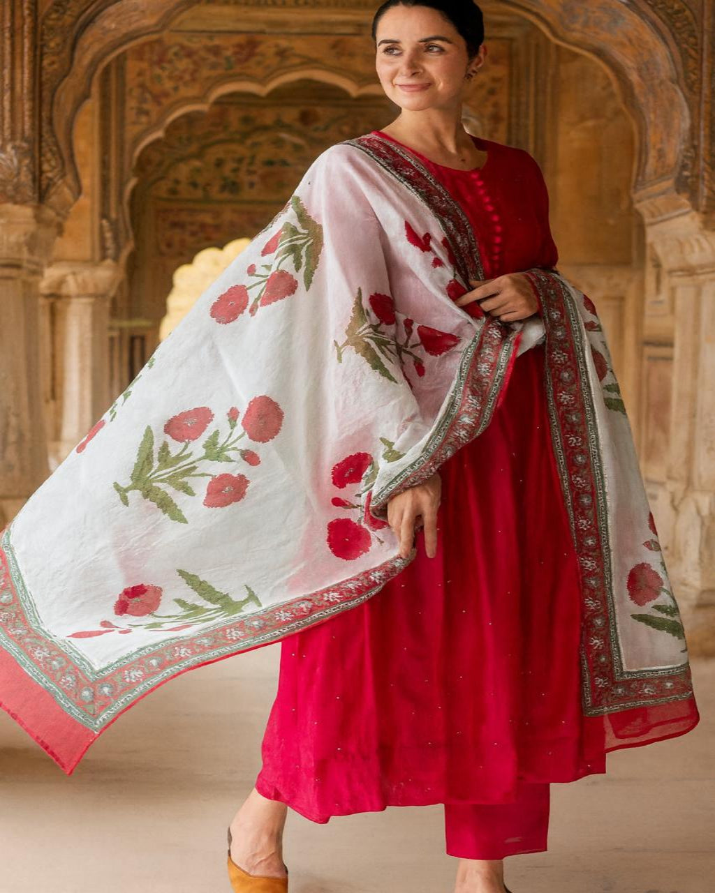 Woman wearing a red traditional outfit with a floral shawl in an ornate architectural setting