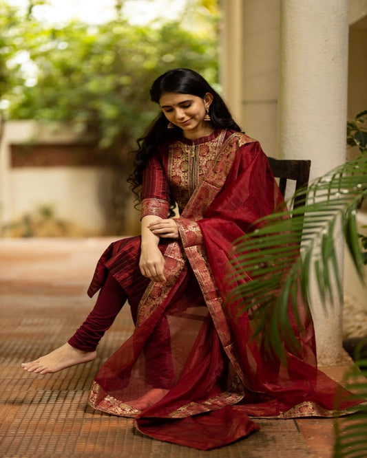 Woman in a traditional red and gold saree sitting outdoors.