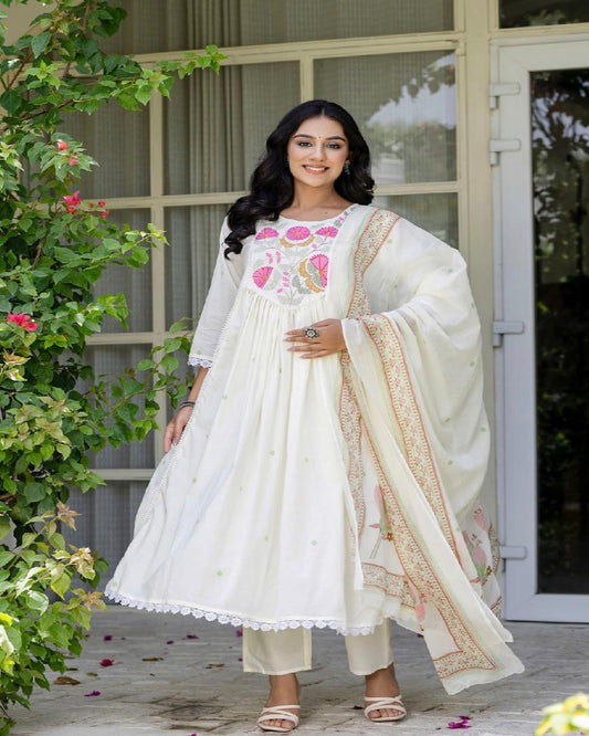 Woman in a white traditional outfit with floral embroidery standing outdoors.