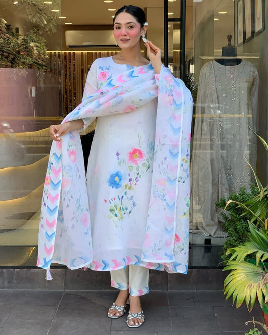 Woman in a white outfit with floral patterns standing in front of a store window.