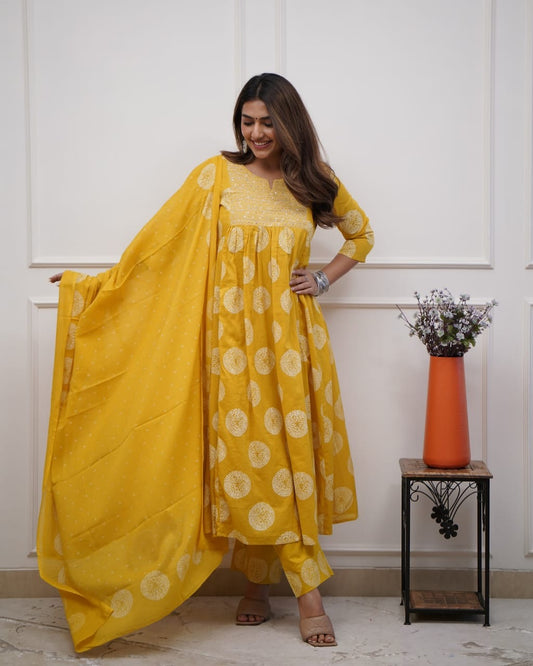 Woman wearing a yellow traditional outfit with a white floral pattern, standing indoors.
