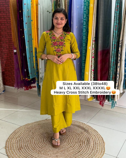 Woman wearing a yellow embroidered outfit standing in front of colorful fabric curtains.