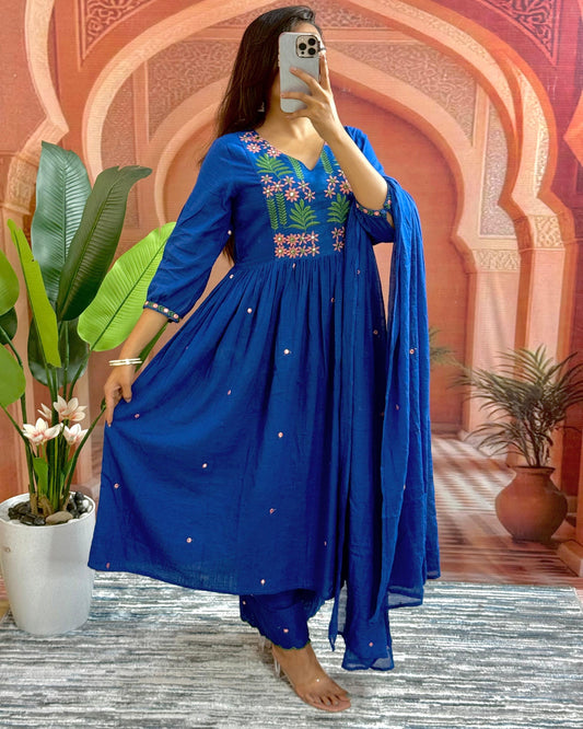 Woman taking a mirror selfie wearing a blue embroidered outfit with a decorative background.