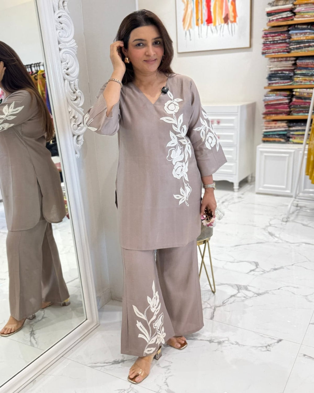 Woman in a gray outfit with white embroidery standing in front of a mirror.
